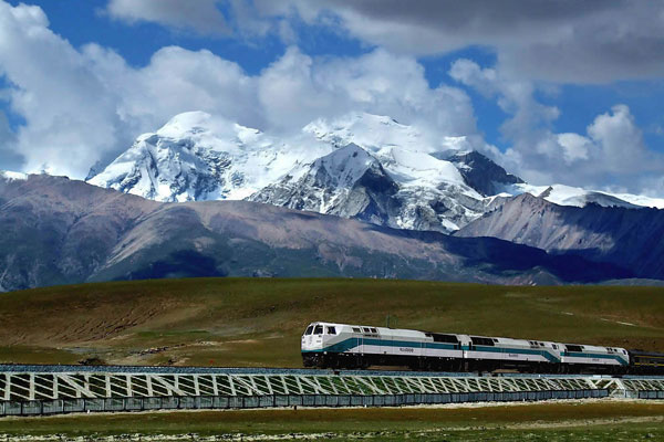 Train speeding on the Qinghai-Tibet Plateau with snow-clad mountains behind